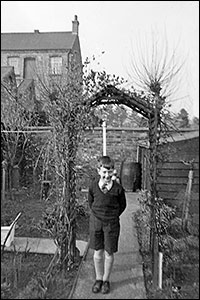 Photograph of Neville in the garden, showing the Ideal Clothing Factory next door.